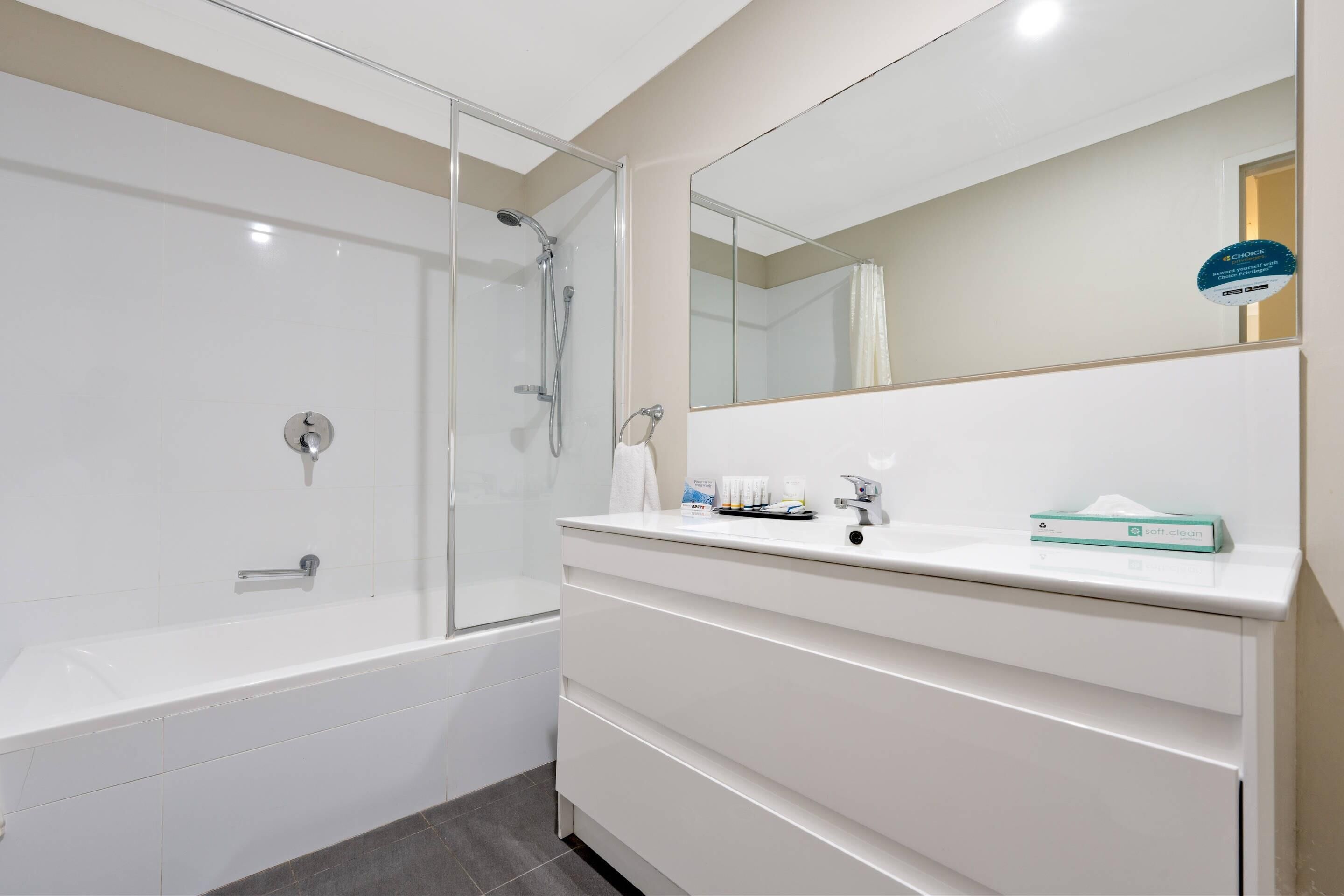 Un baño moderno con ducha de vidrio, bañera blanca y tocador con espejo y artículos de aseo.