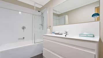 Un baño moderno con ducha de vidrio, bañera blanca y tocador con espejo y artículos de aseo.