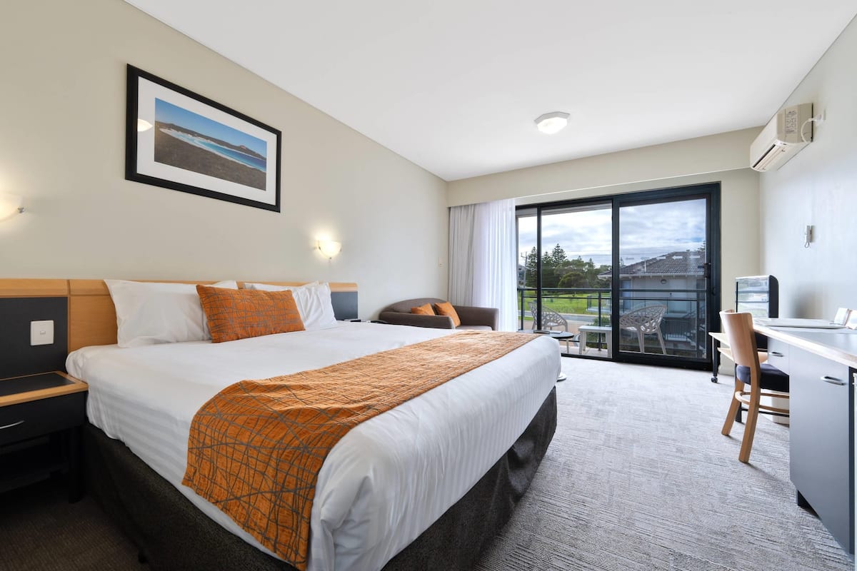 A hotel room with a large bed, a desk, and a view of the outdoors.