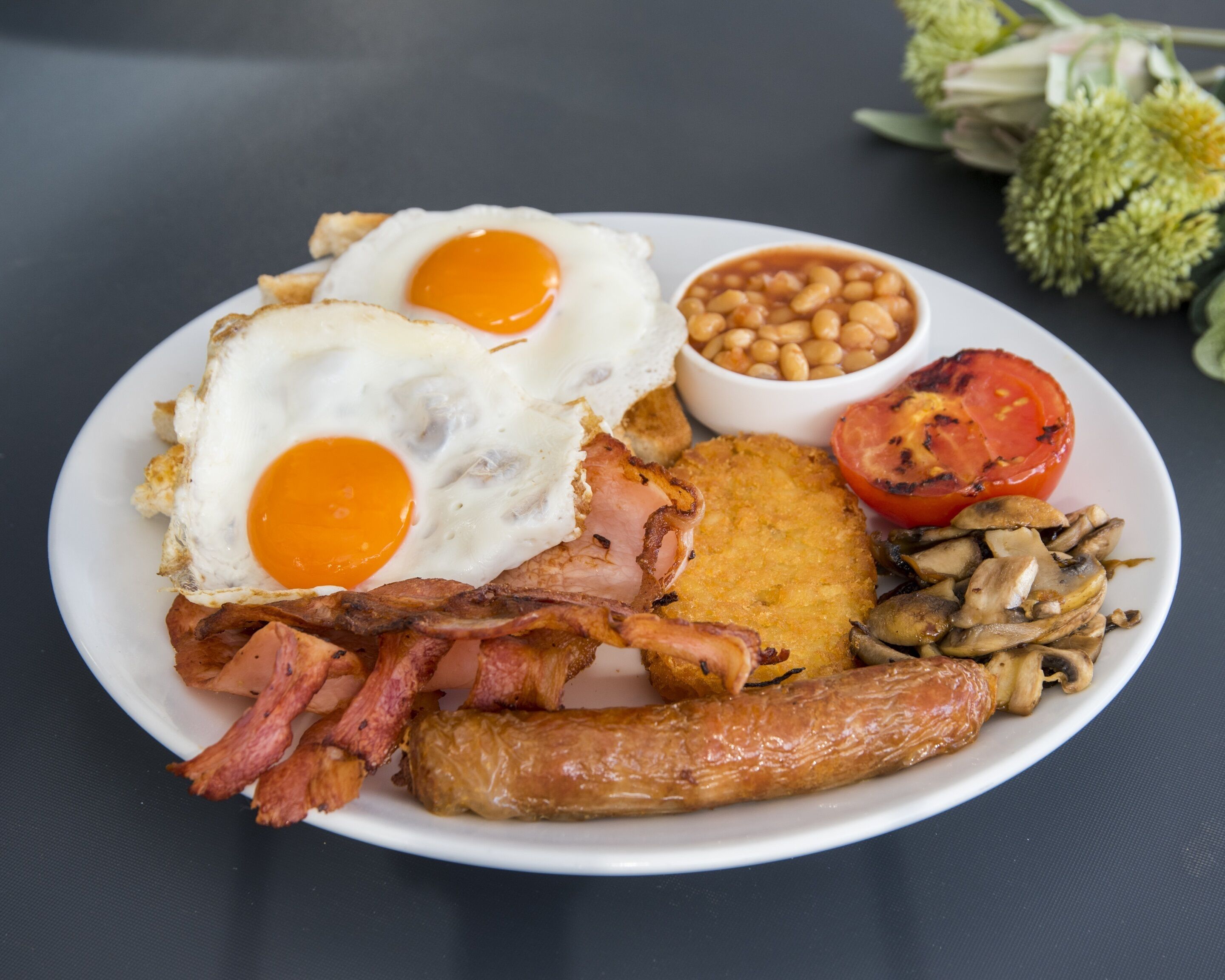 Un plato de comida para el desayuno con huevos, tocino, salchichas, champiñones, frijoles y tomate a la parrilla.