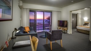 A hotel room with a balcony, a TV, a desk, and a bed.