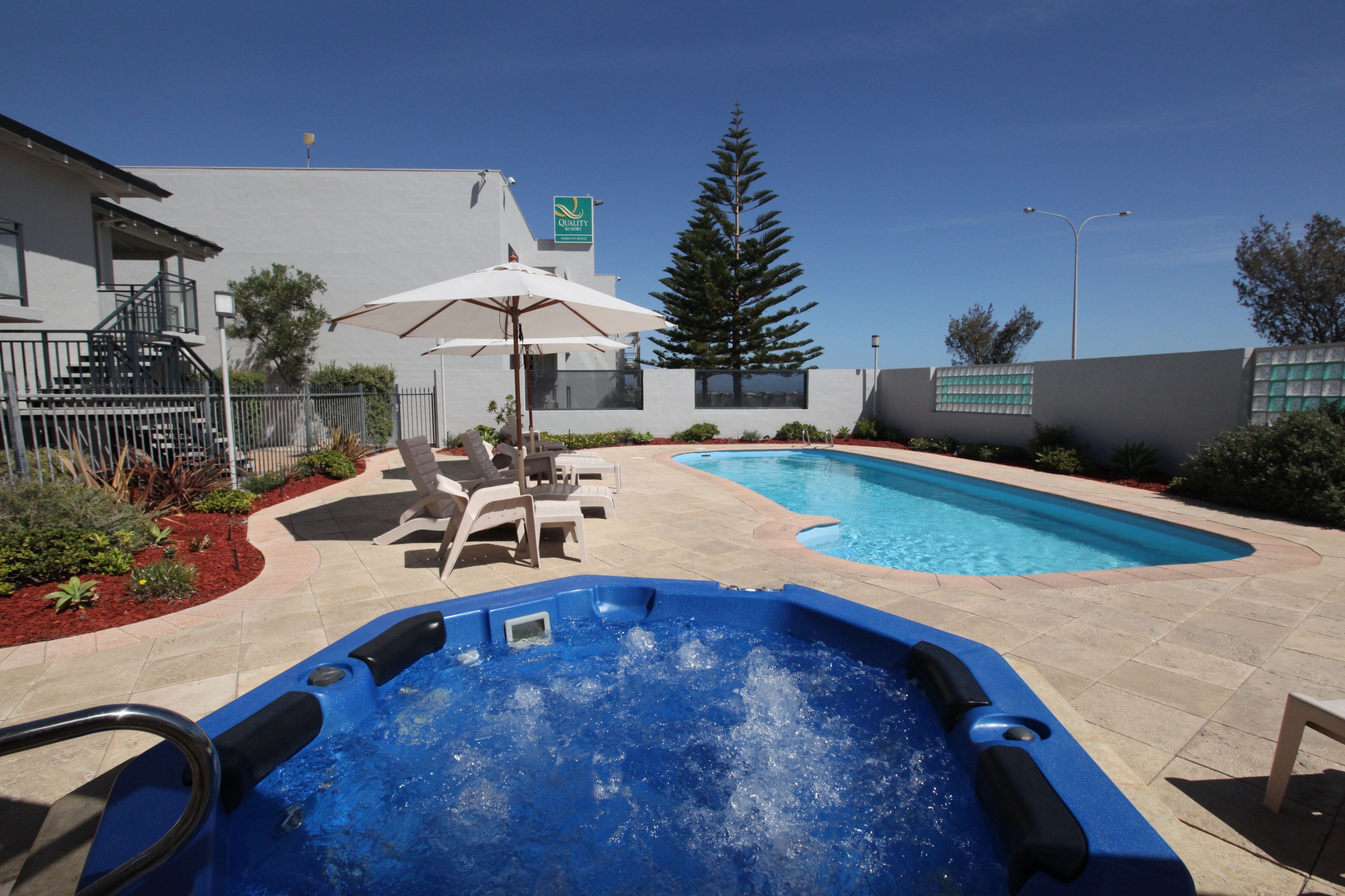 Una piscina con hidromasaje, sillas de descanso y una zona con sombrillas.