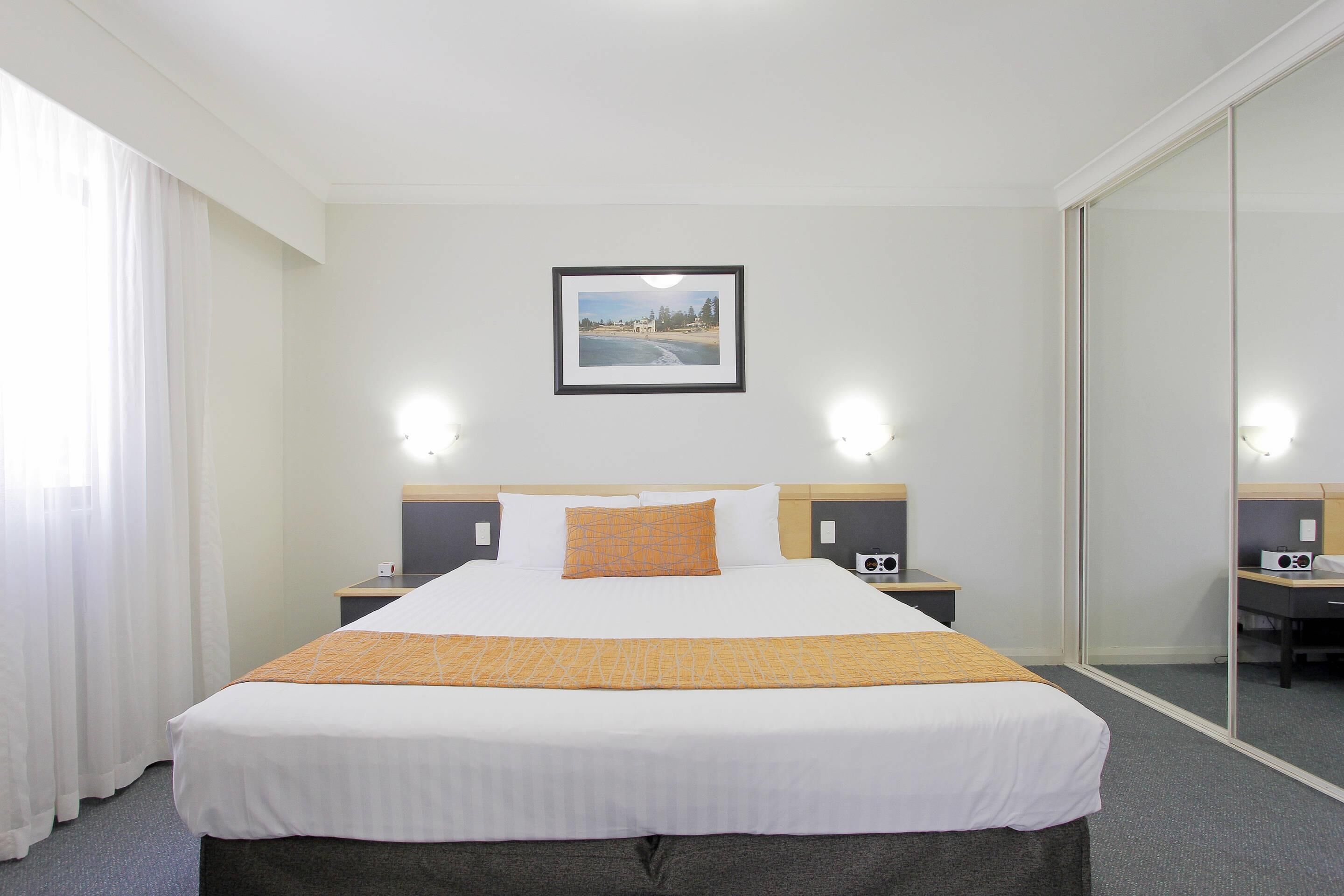 A hotel room with a large bed, a bedside table with a radio, a framed picture on the wall, and a mirror on the door.