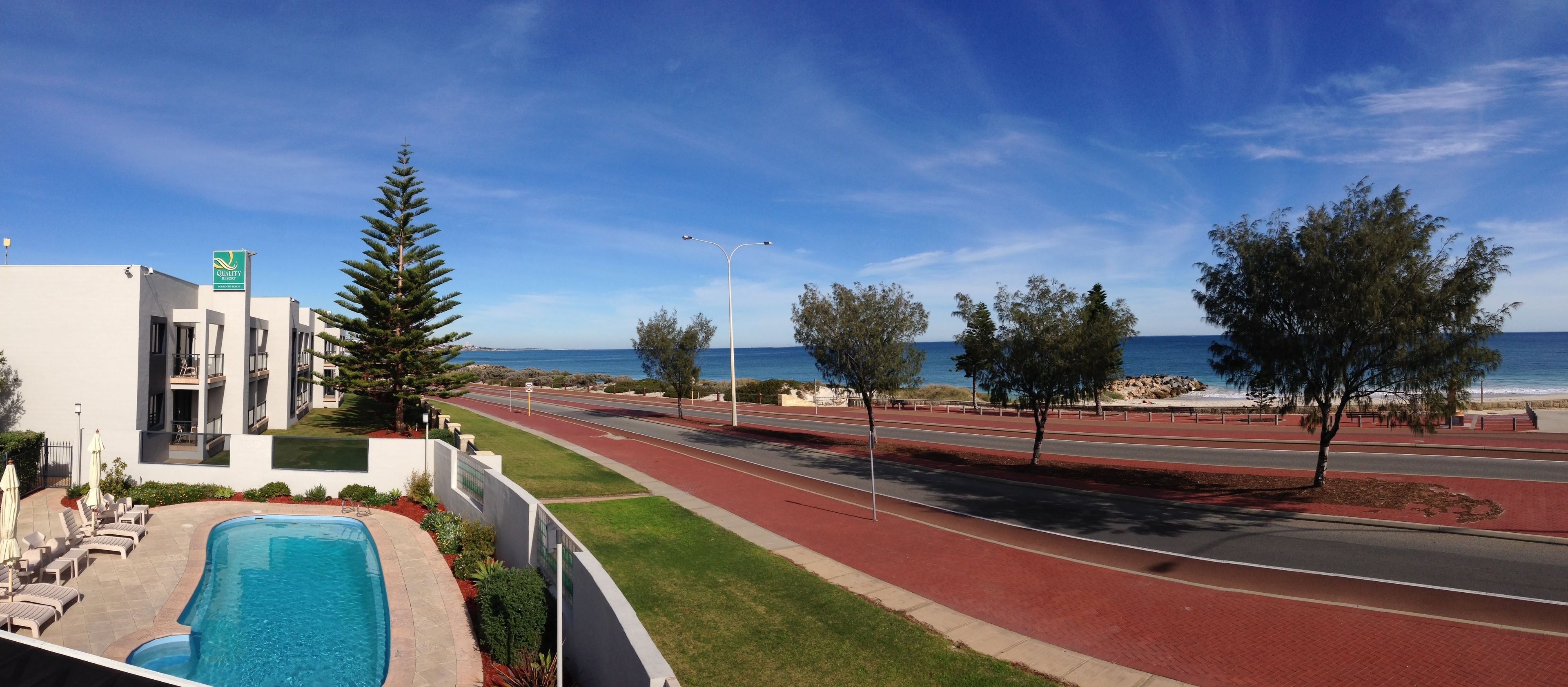 A hotel with a swimming pool, a road with a red bike lane, and a view of the ocean.