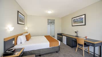 A hotel room with a bed, desk, chair, and a small kitchenette.