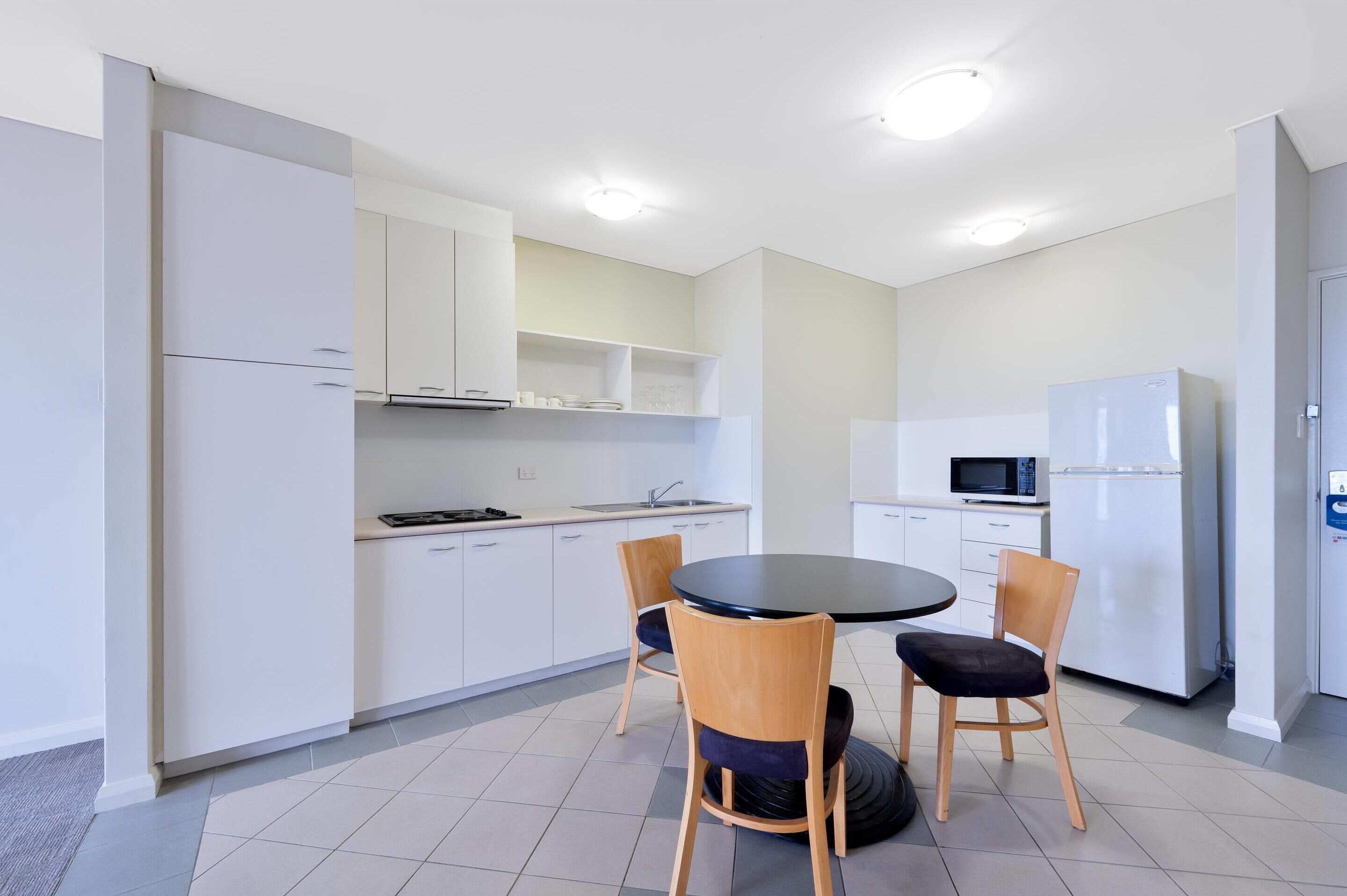 Una cocina moderna con armarios blancos, un comedor negro y dos sillas de madera.