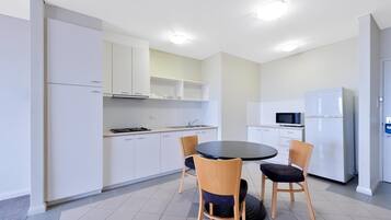 Una cocina moderna con armarios blancos, un comedor negro y dos sillas de madera.