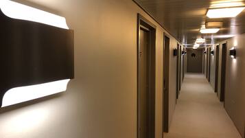 A hallway with multiple doors, some with handles and others with keypads, and a wall-mounted light fixture on the left.