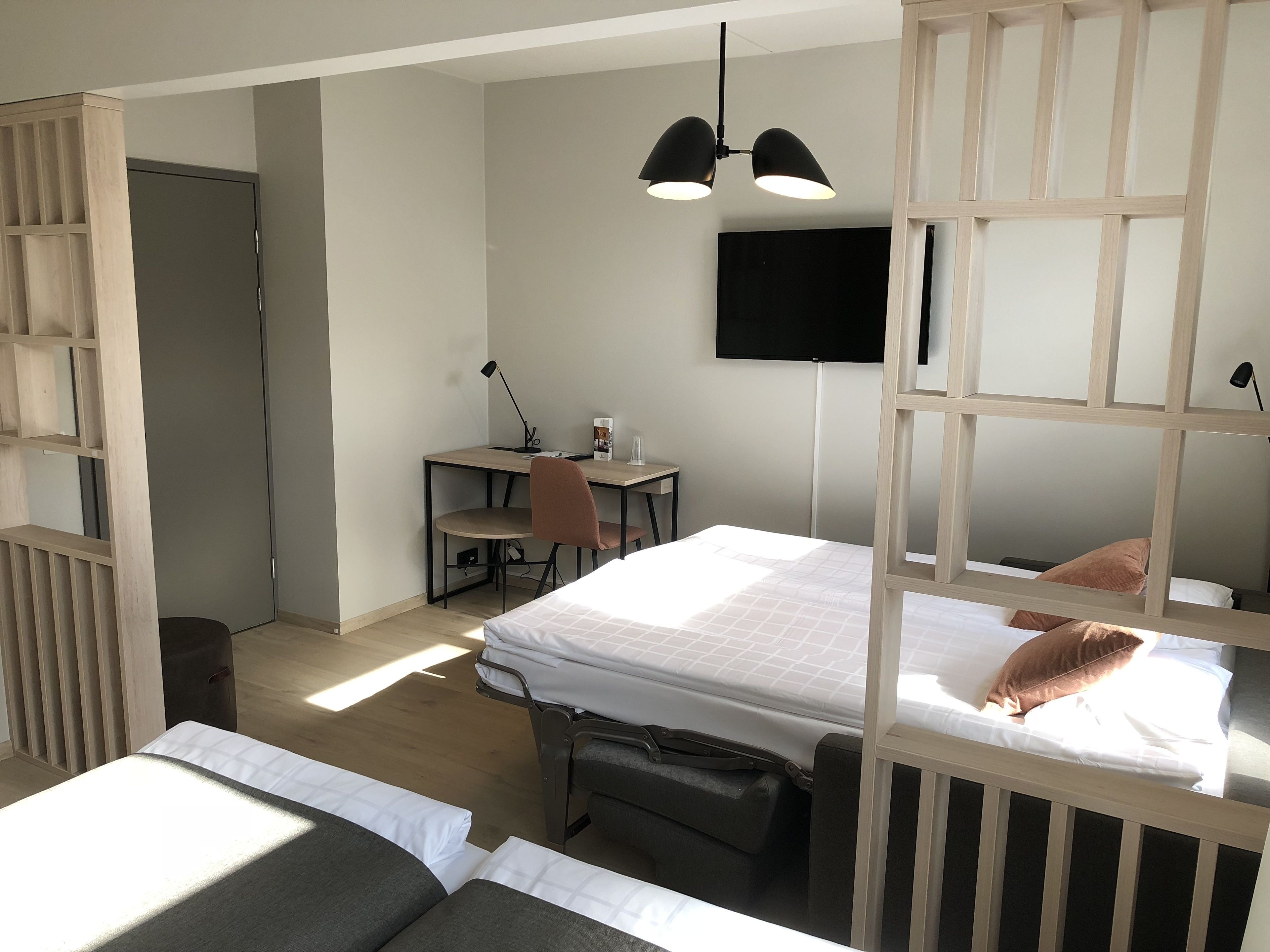A modern hotel room with a bed, desk, chair, and a TV mounted on the wall.