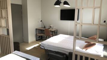 A modern hotel room with a bed, desk, chair, and a TV mounted on the wall.