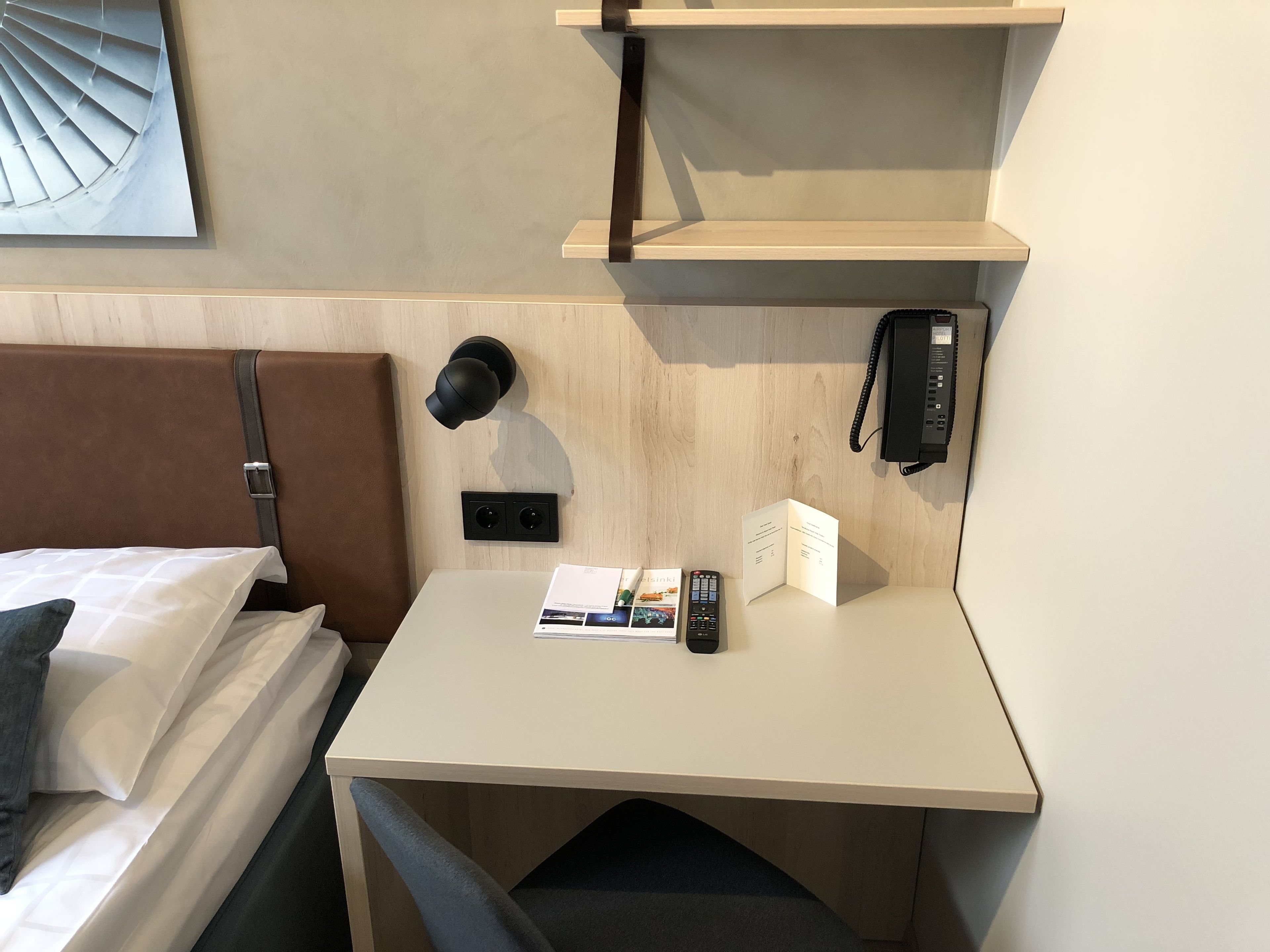 Ein Hotelzimmer mit einem Bett, einem Schreibtisch, einem Telefon und einer Wandlampe.