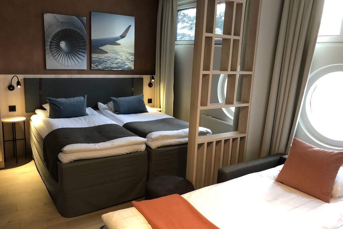 A modern hotel room with two beds, a large window, and artwork on the wall.