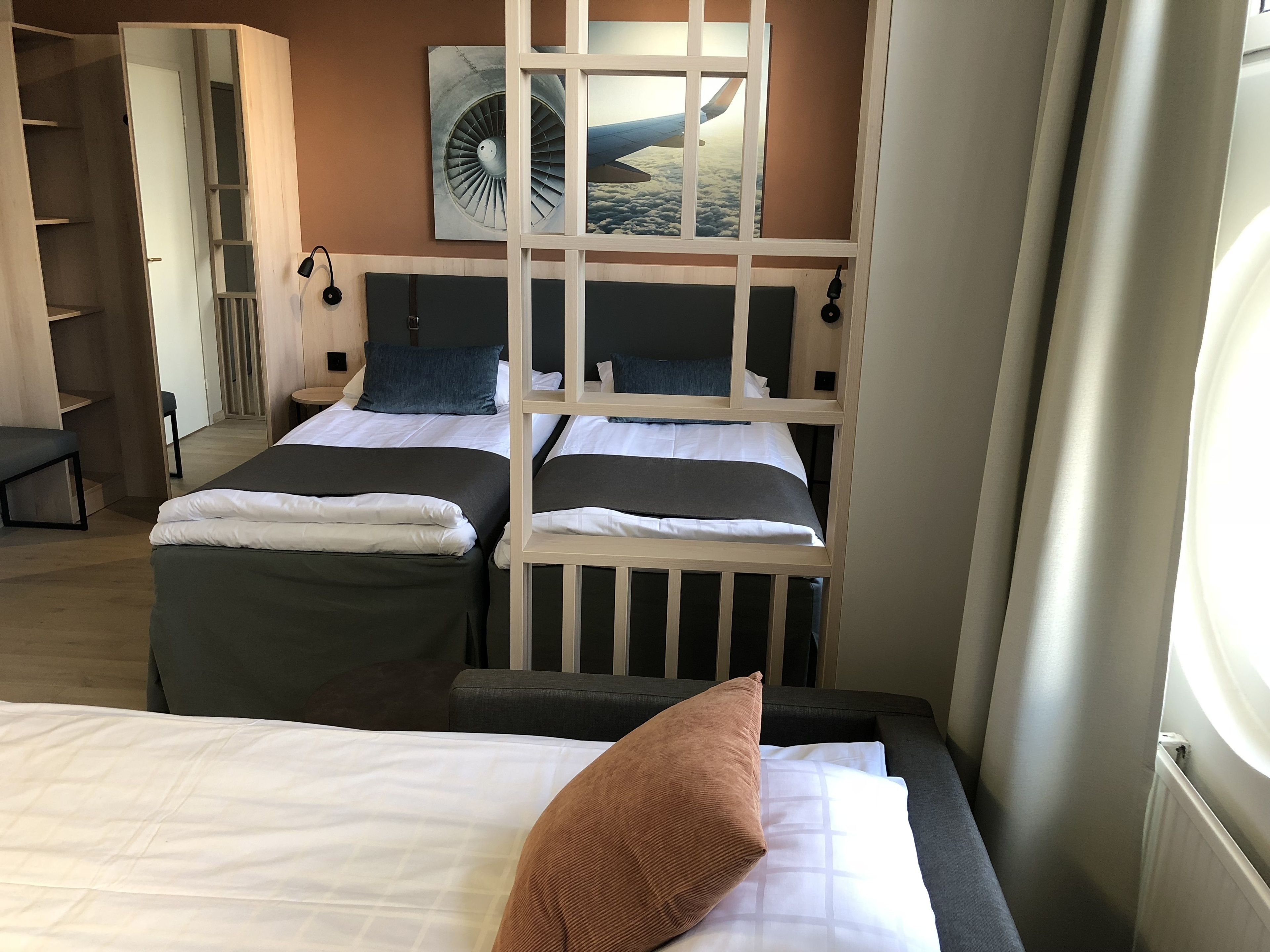 Habitación de hotel con dos camas, vista del cielo a través de una ventana y un armario de madera.