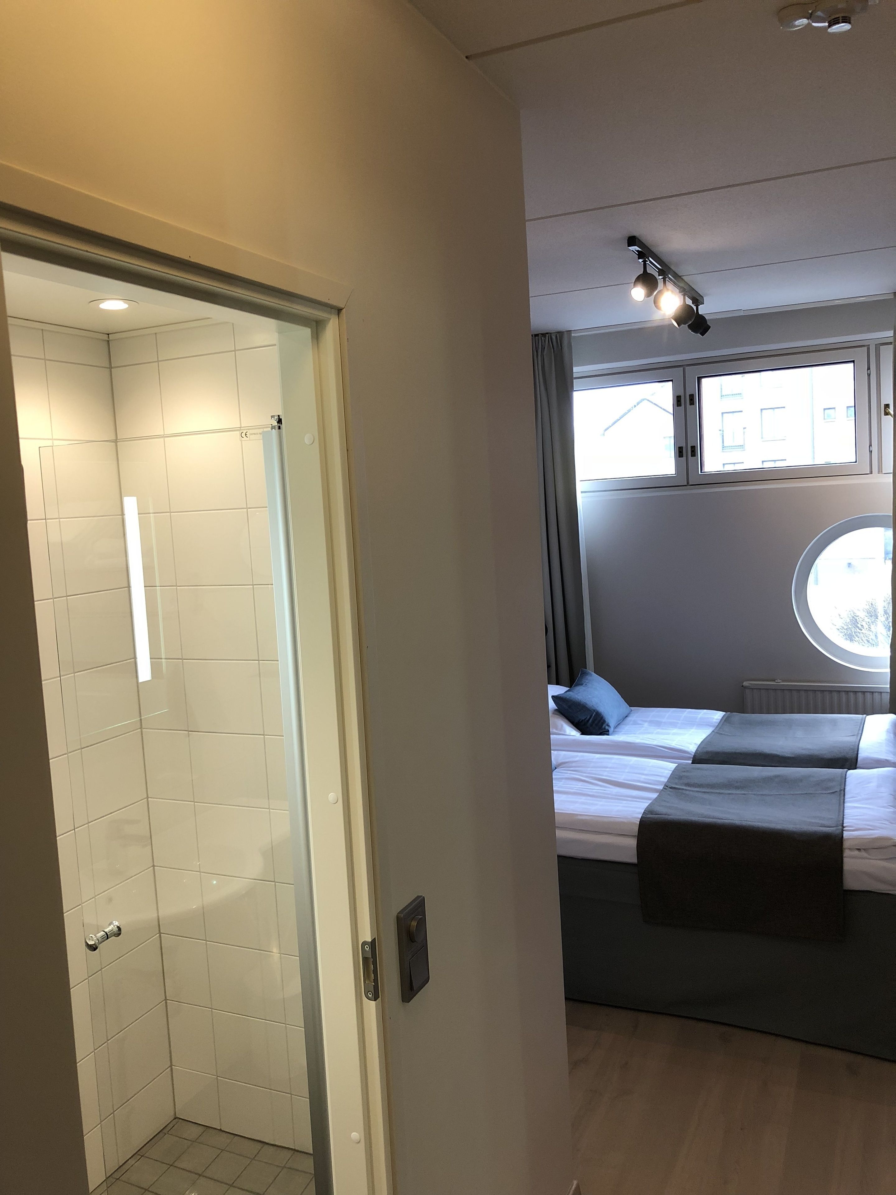 Habitación de hotel moderna con ducha, una cama con dos almohadas, ventana con vistas y una lámpara de techo.
