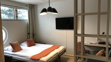 Habitación de hotel con cama, escritorio, silla, televisión y ventana con cortinas.