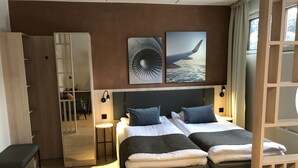 Una habitación de hotel moderna con una cama grande, dos mesitas de noche, un espejo y una obra de arte que representa un ala de avión y un ventilador.