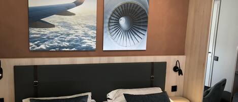 Habitación de hotel con dos camas, un ventanal grande y obra de arte que representa un ala de avión y un motor.
