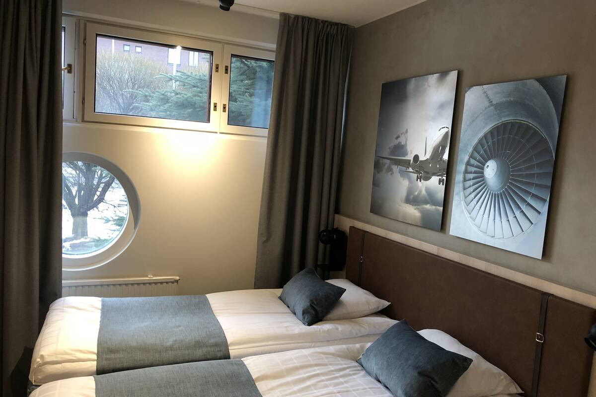 A hotel room with two beds, a window with curtains, and two wall-mounted pictures.