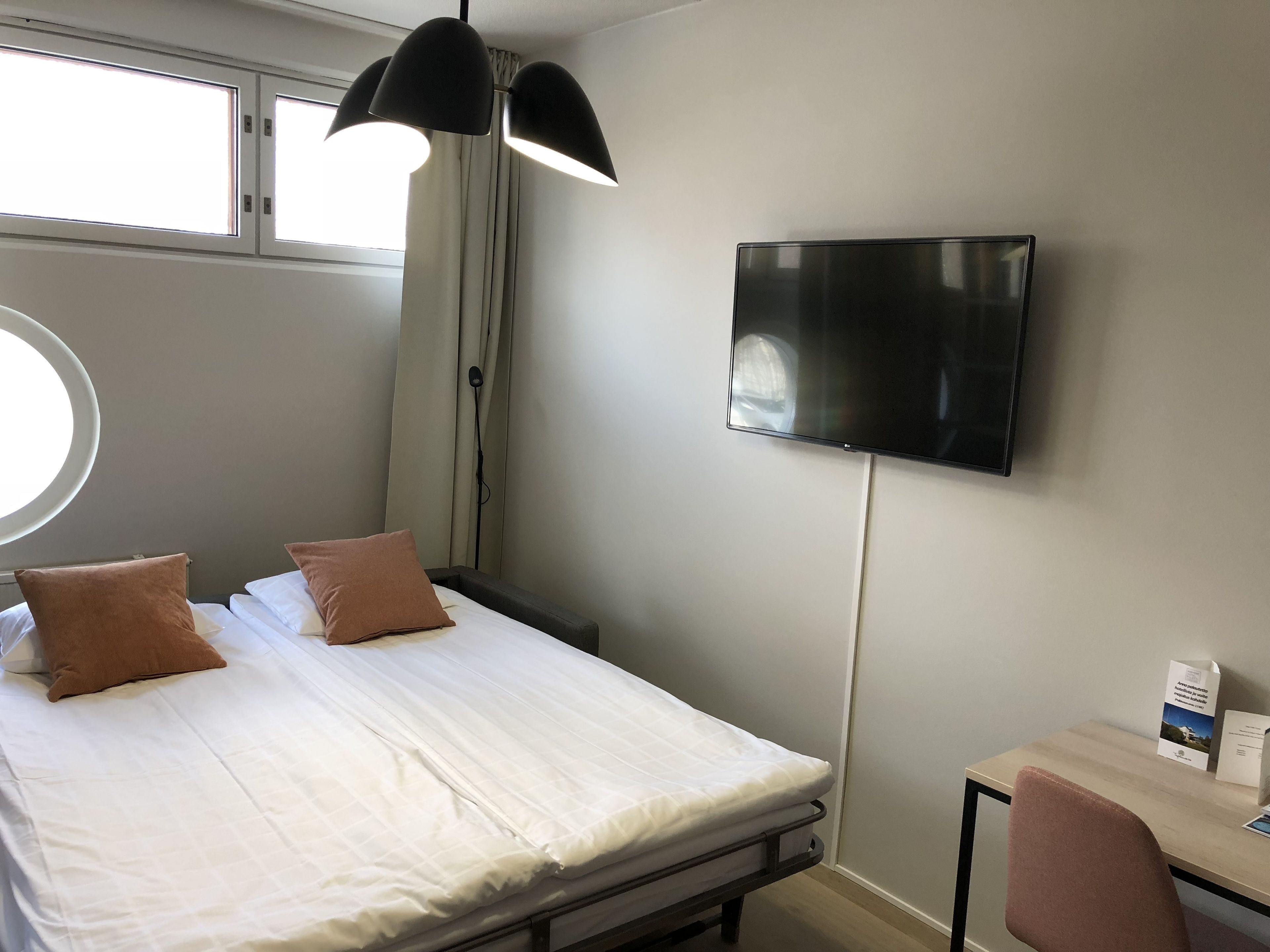 Una habitación de hotel con cama, escritorio, televisor y ventana.