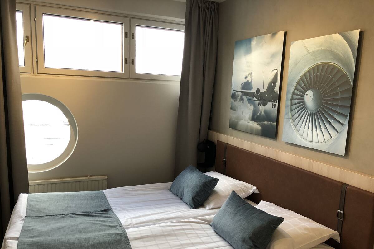 A hotel room with a bed, a round window, and two wall-mounted artworks.