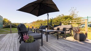 A wooden deck with outdoor furniture, including a sofa and chairs, a table, and a large umbrella. - Good Morning Mölndal (Mölndal)