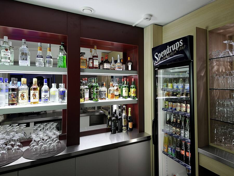 Zona de bar con estantes llenos de botellas de licor y un expositor refrigerado.