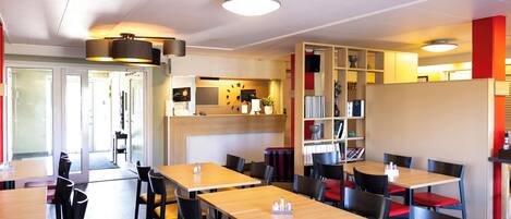 Restaurante moderno com mesas e cadeiras de madeira, um balcão de recepção e uma estante de livros.