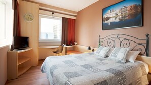 A hotel room with a bed, a TV, a desk, a chair, a window with curtains, a clock, and a painting on the wall. - ibis Lodz Centrum (Lodz)