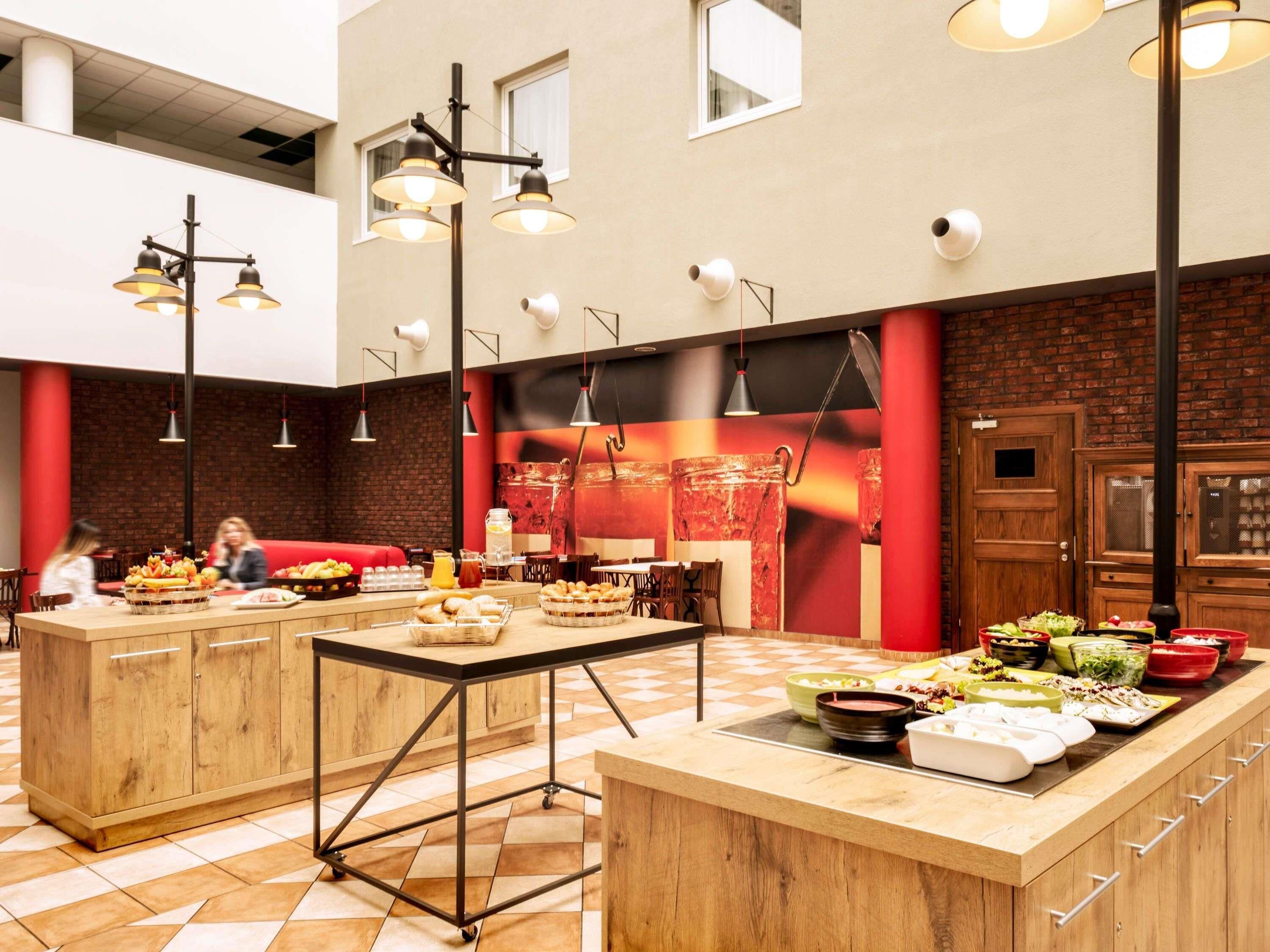 A modern restaurant with a central island serving food, a brick wall, and a mix of hanging and pendant lighting.