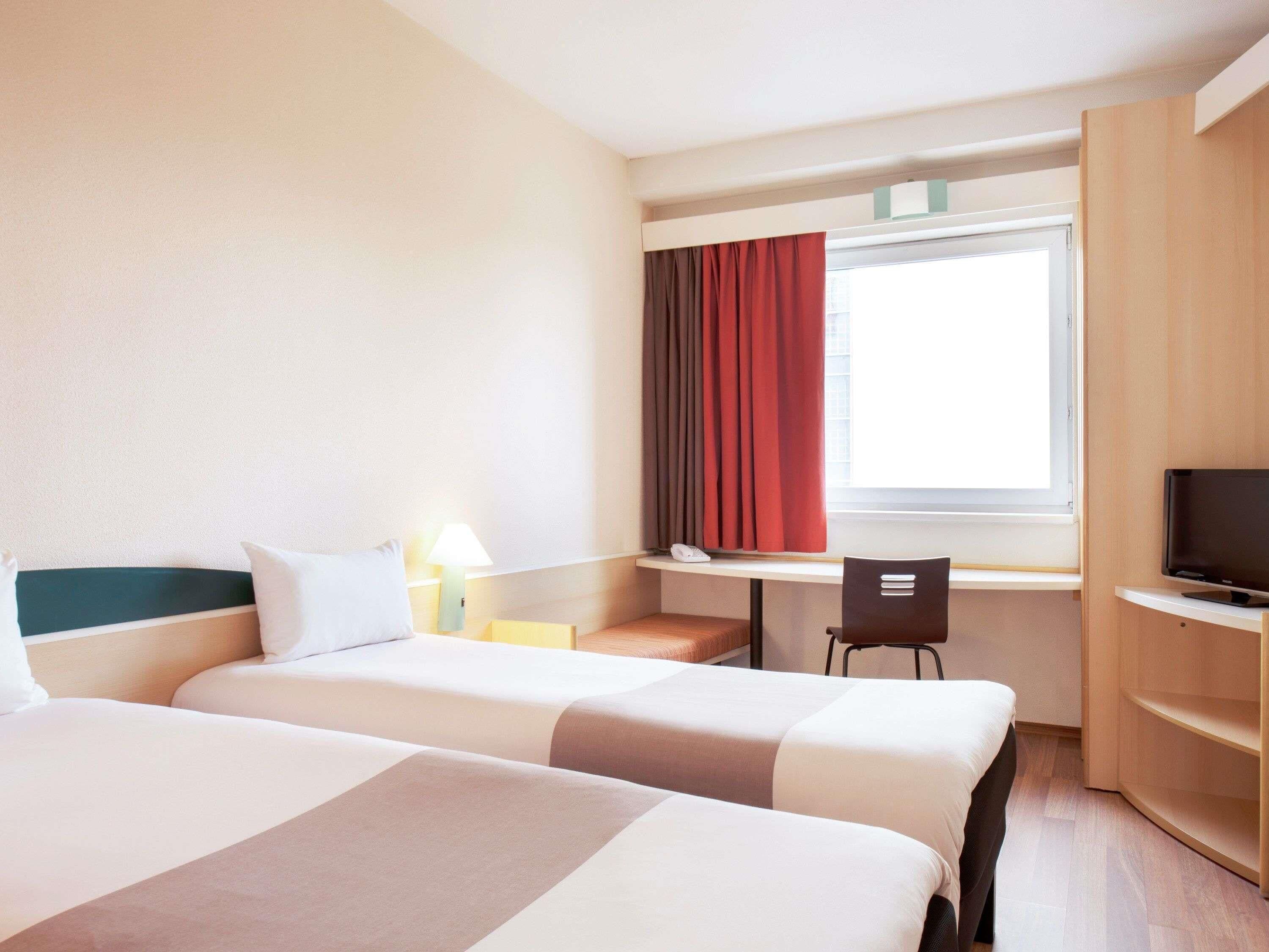 Habitación de hotel con dos camas, un escritorio, una silla, un televisor y una ventana con cortinas.