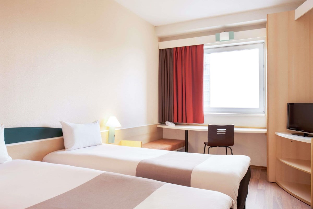 Habitación de hotel con dos camas, un escritorio, una silla, un televisor y una ventana con cortinas.