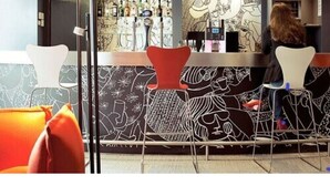 A bar area with a counter, bar stools, and a patterned wall. - ibis Lodz Centrum (Lodz)