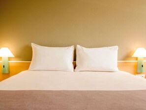 A hotel room with a bed, two bedside lamps, and a plain wall. - ibis Lodz Centrum (Lodz)