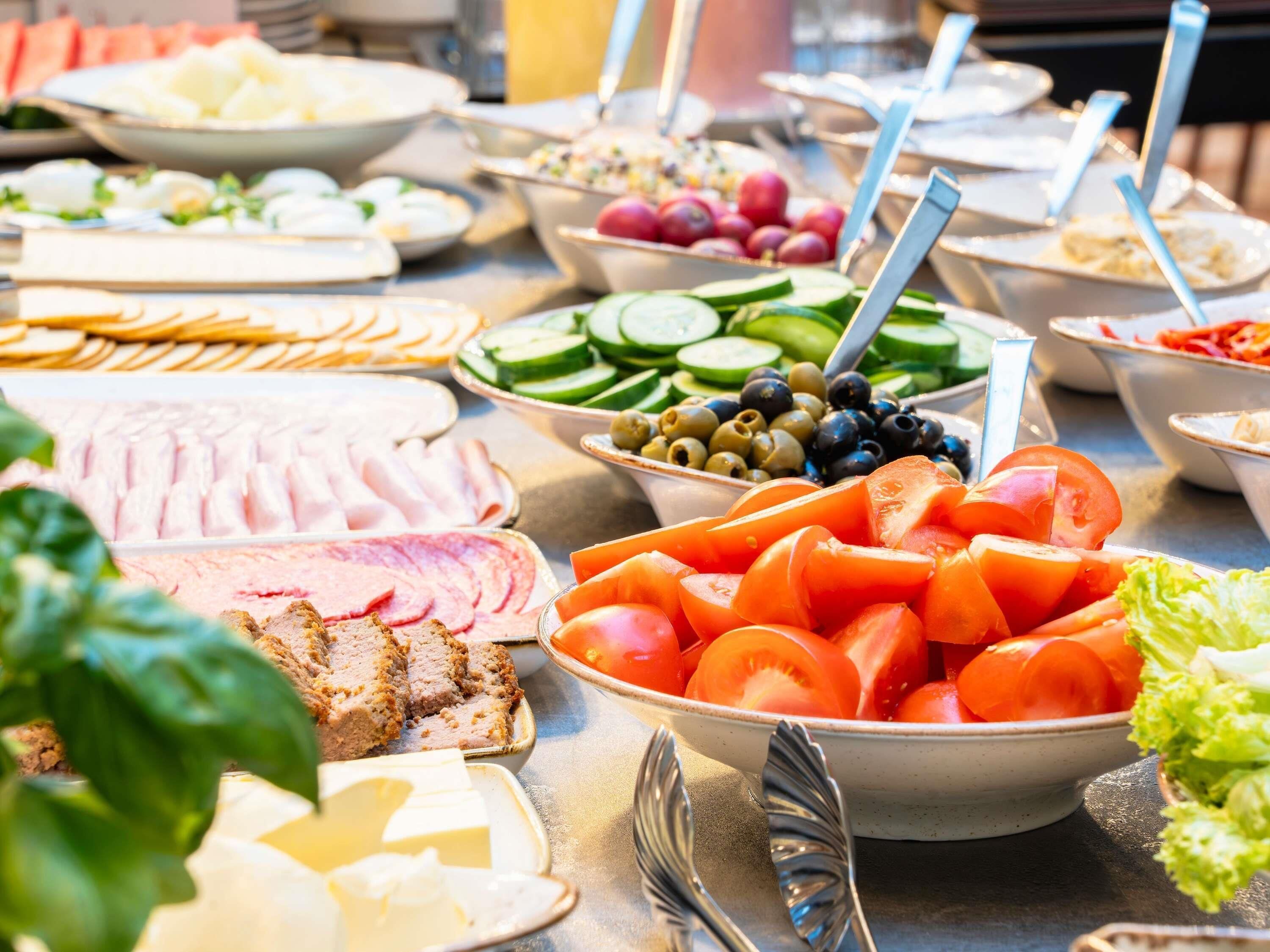 A buffet with various food items including sliced meats, cheeses, vegetables, and fruits.