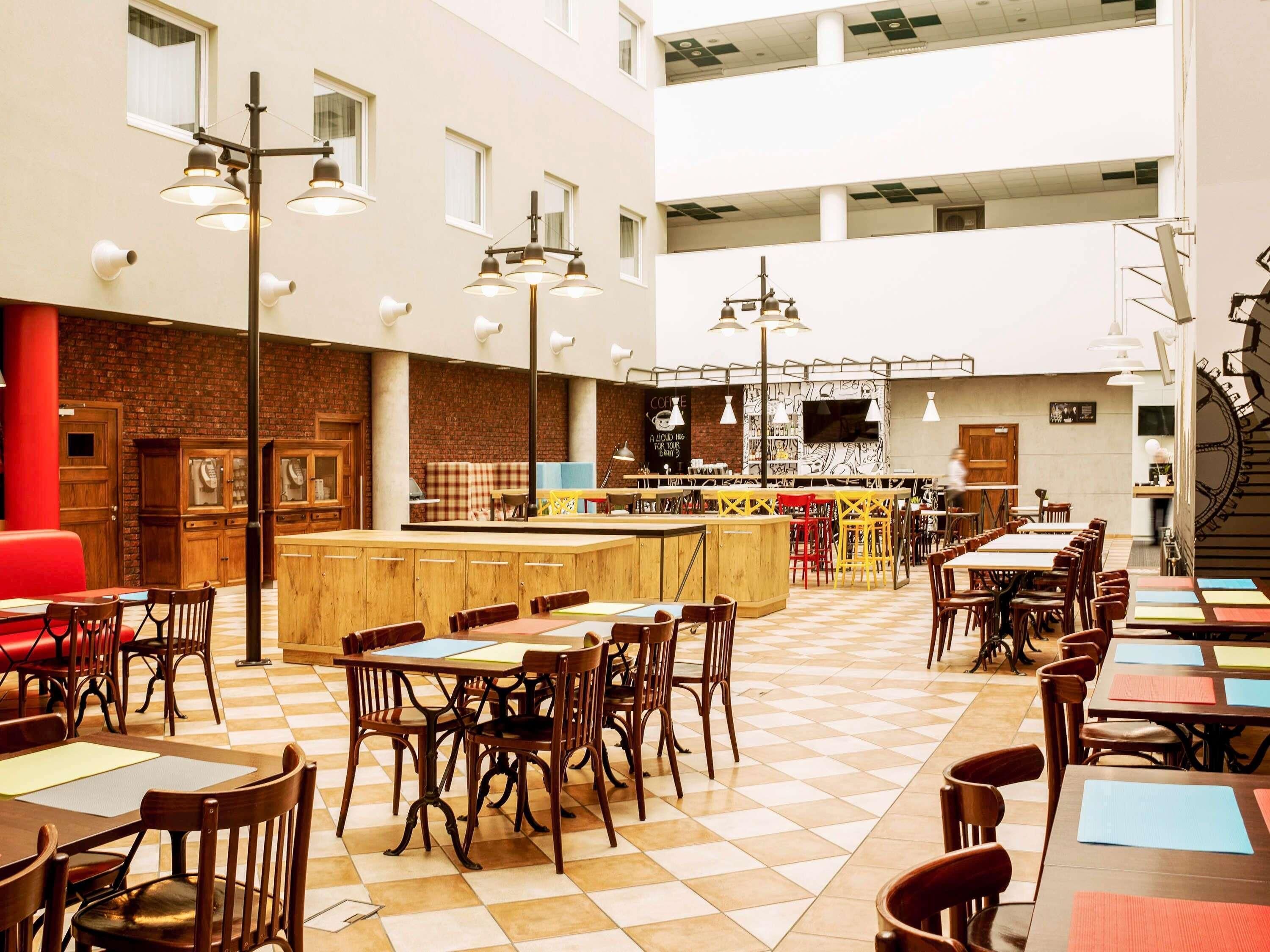 Un vaste espace intérieur aménagé en salle à manger, avec de nombreuses tables et chaises, un bar central et un plafond haut avec des poutres apparentes.