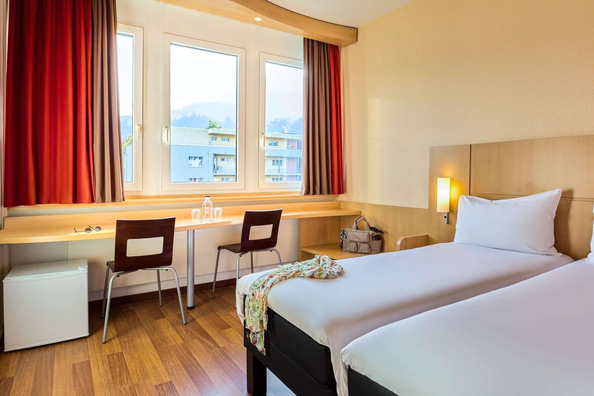 Une chambre d’hôtel équipée d’un lit, d’un bureau, de chaises, d’un petit réfrigérateur et d’une fenêtre avec des rideaux.