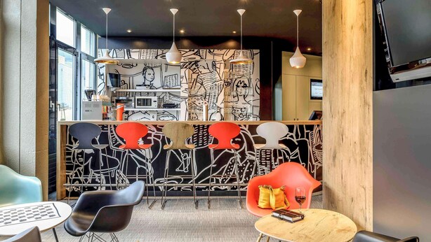 Un área de bar moderna con un mural blanco y negro único, sillas negras y rojas, y una barra de madera.