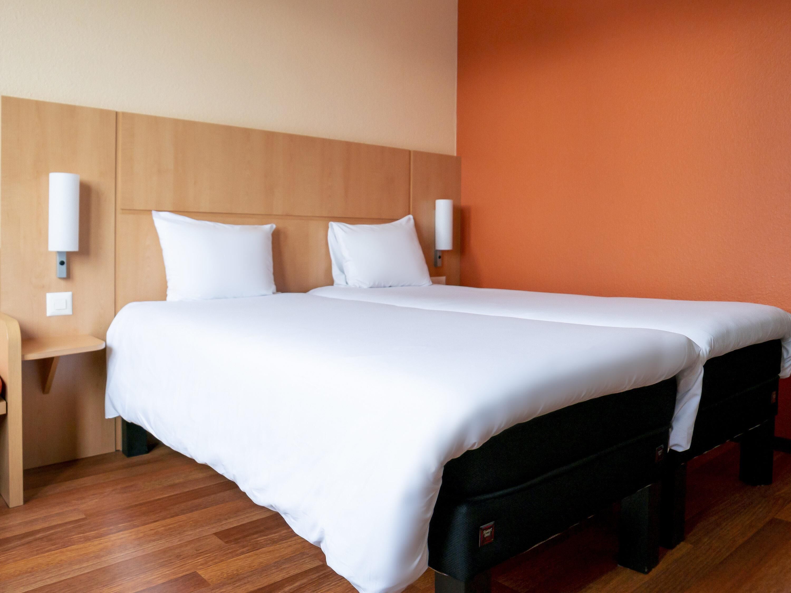 Una habitación de hotel con una cama grande, cabecera de madera, dos mesitas de noche y una lámpara de pared.