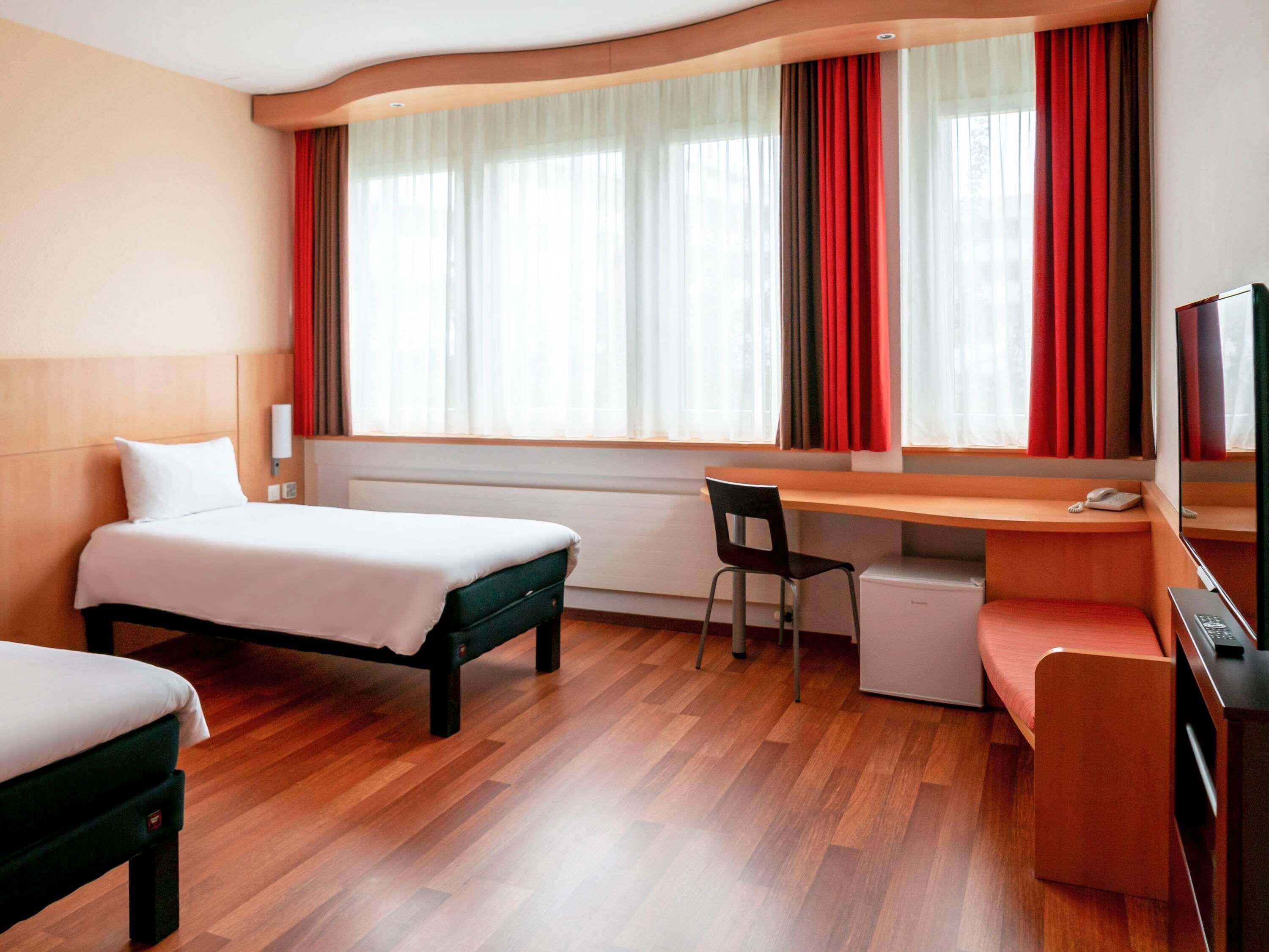 A hotel room with a bed, desk, chair, and a small kitchenette.