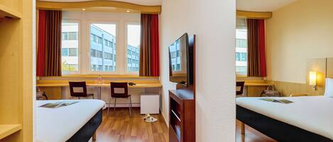A hotel room with two beds, a desk, a chair, a television, and a window with curtains.