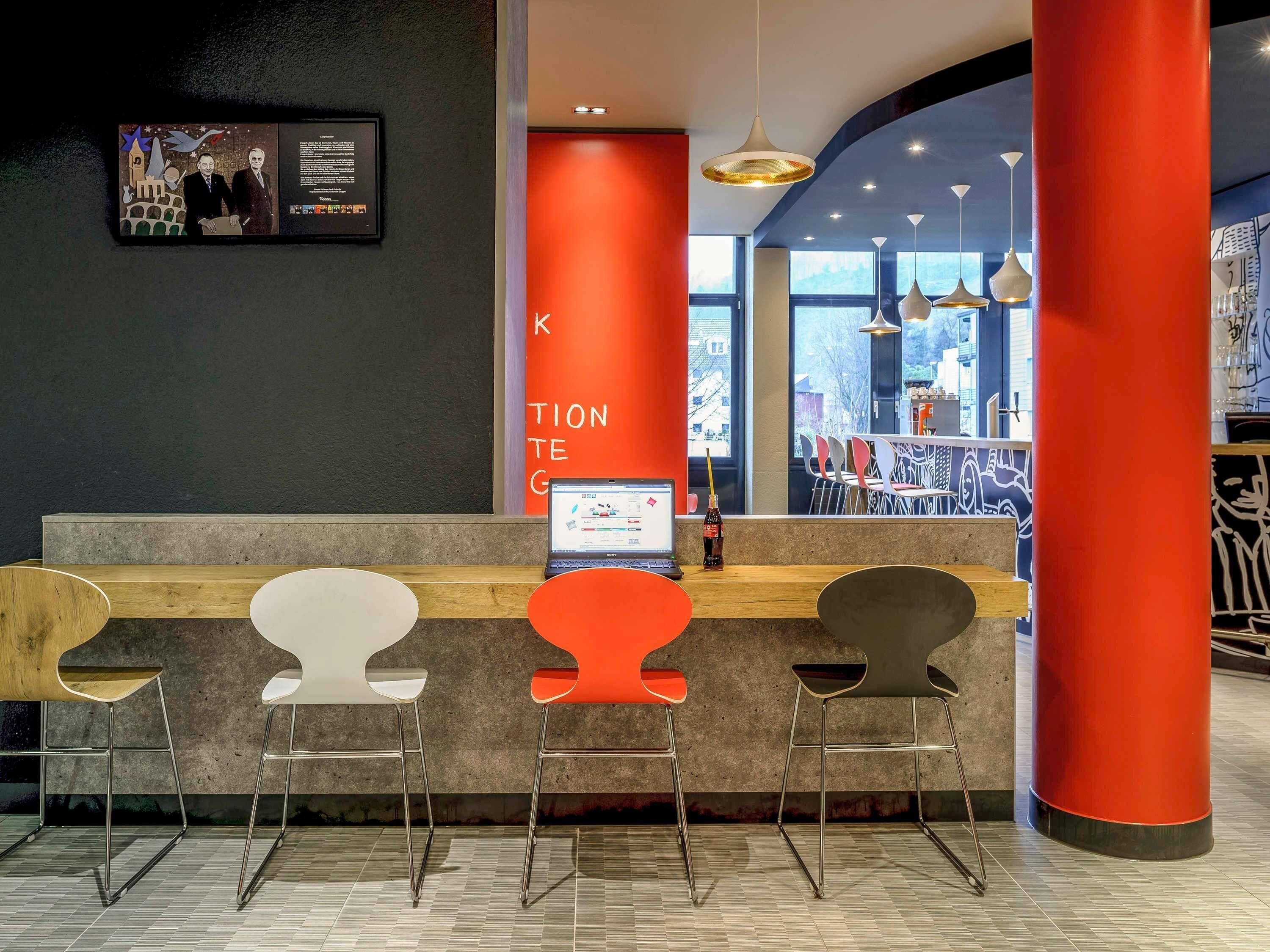 A reception area with a counter, three chairs, a laptop, and a wall-mounted screen.