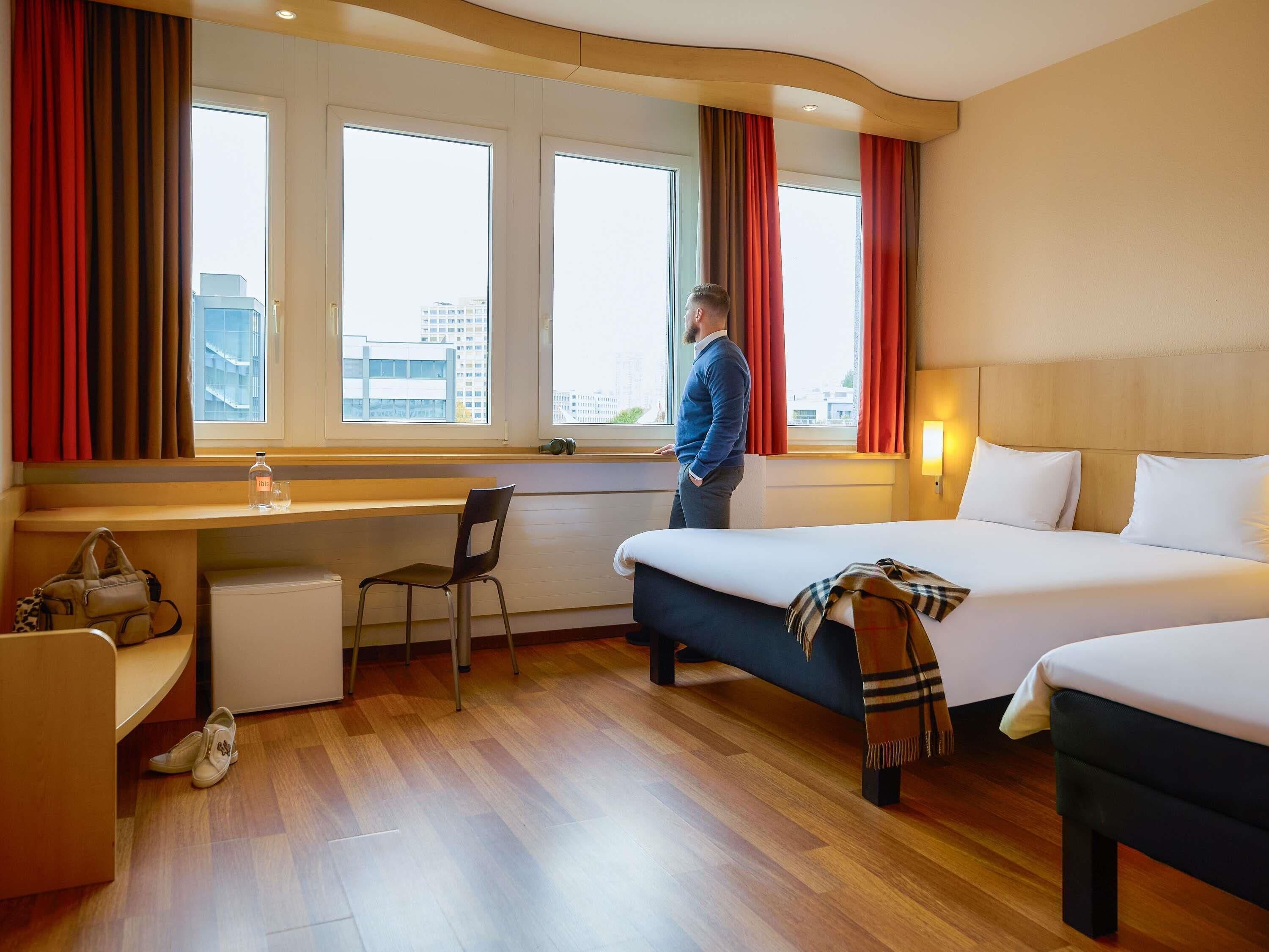 A hotel room with a bed, a desk, a chair, a small table, and a window with curtains.