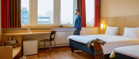 Una habitación de hotel con cama, escritorio, silla, mesita y ventana con cortinas.