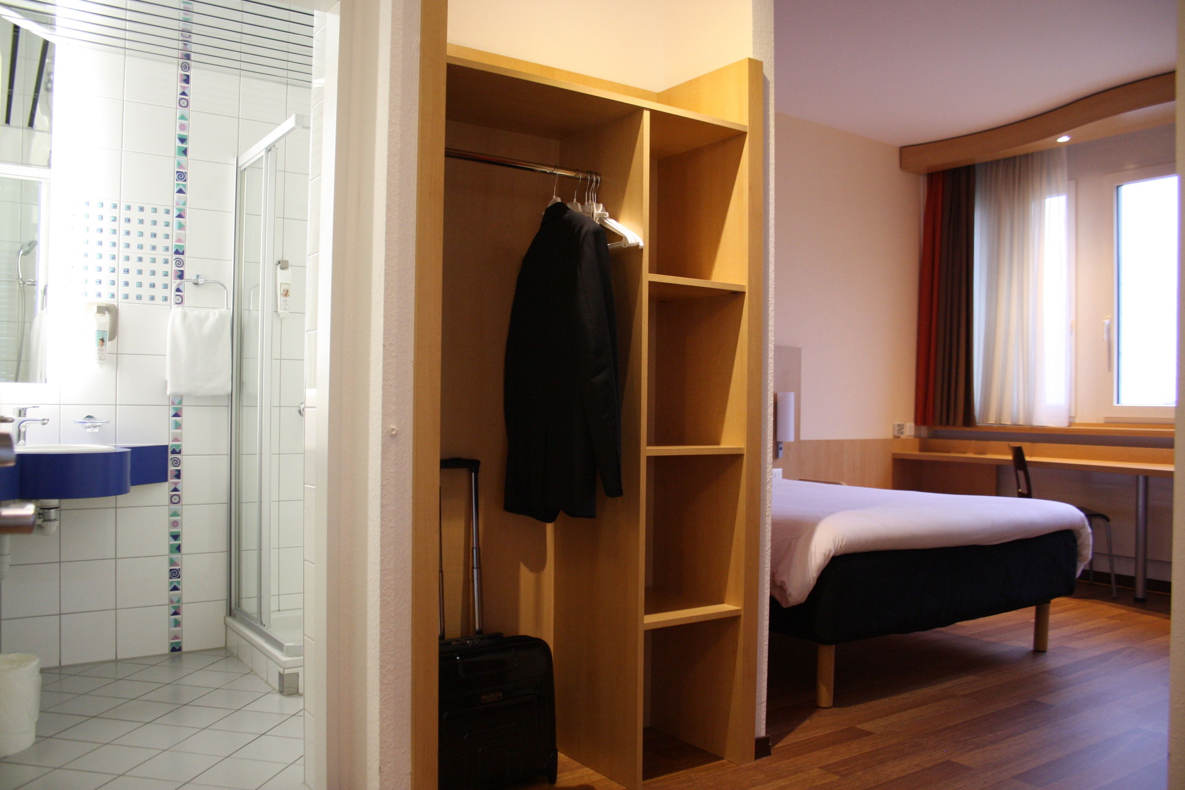 Een hotelkamer met een douche, een bed, een bureau en een kledingkast.