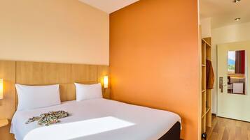 Habitación de hotel con una cama grande, cabecero de madera, dos lámparas de noche y vistas a la montaña a través de una puerta abierta.