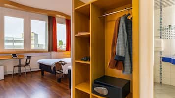 Ein Hotelzimmer mit einem Bett, einem Schreibtisch, einem Kleiderschrank und Blick auf Gebäude durch das Fenster.
