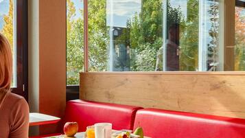 Ein modernes Interieur mit einer roten Lederausstattung, einem Holztisch mit Frühstücksangeboten und Blick auf Bäume und Berge durch große Fenster.