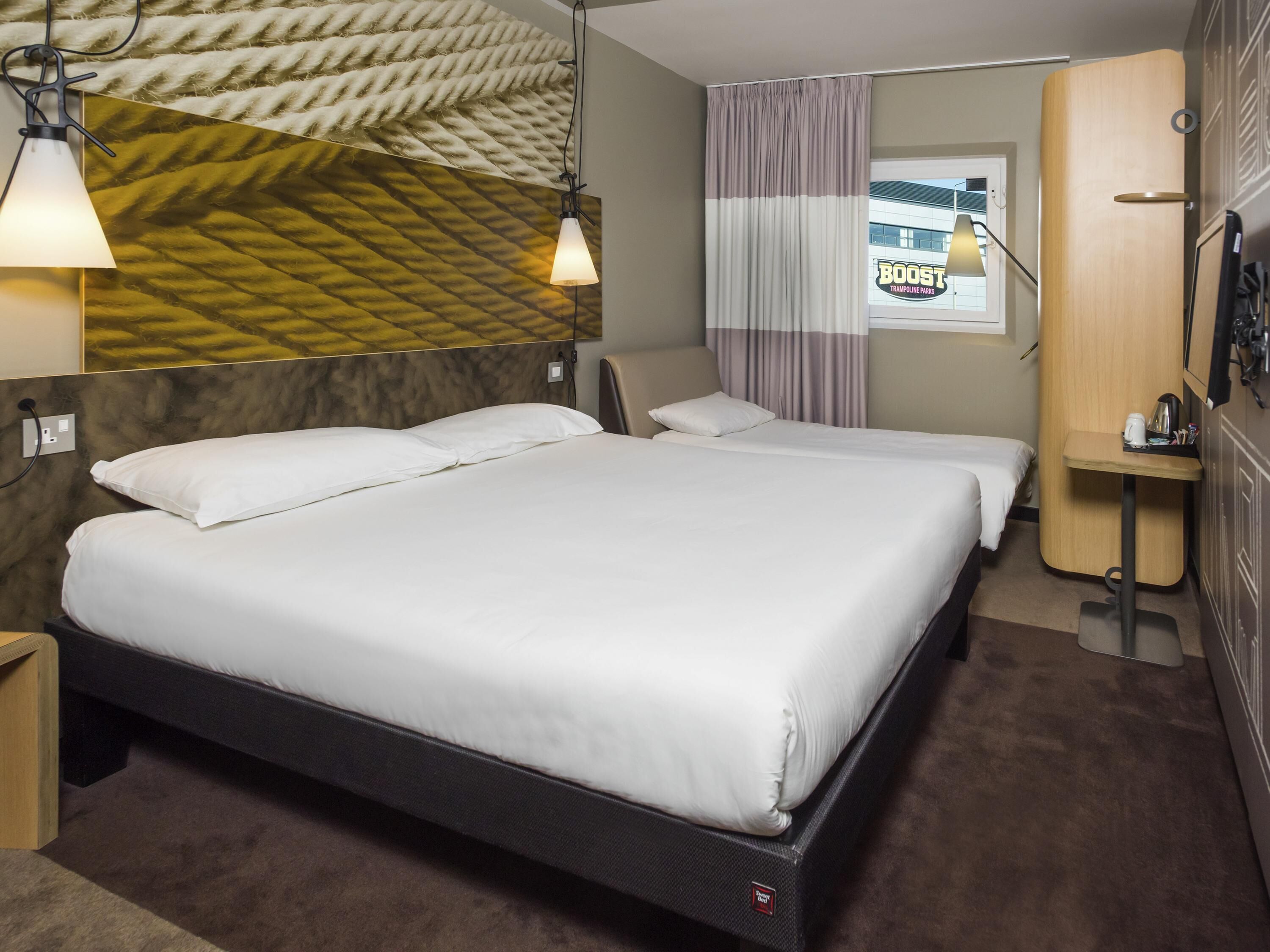 Una habitación de hotel con una cama grande, dos mesitas de noche, un espejo, una ventana con cortinas y un televisor montado en la pared.