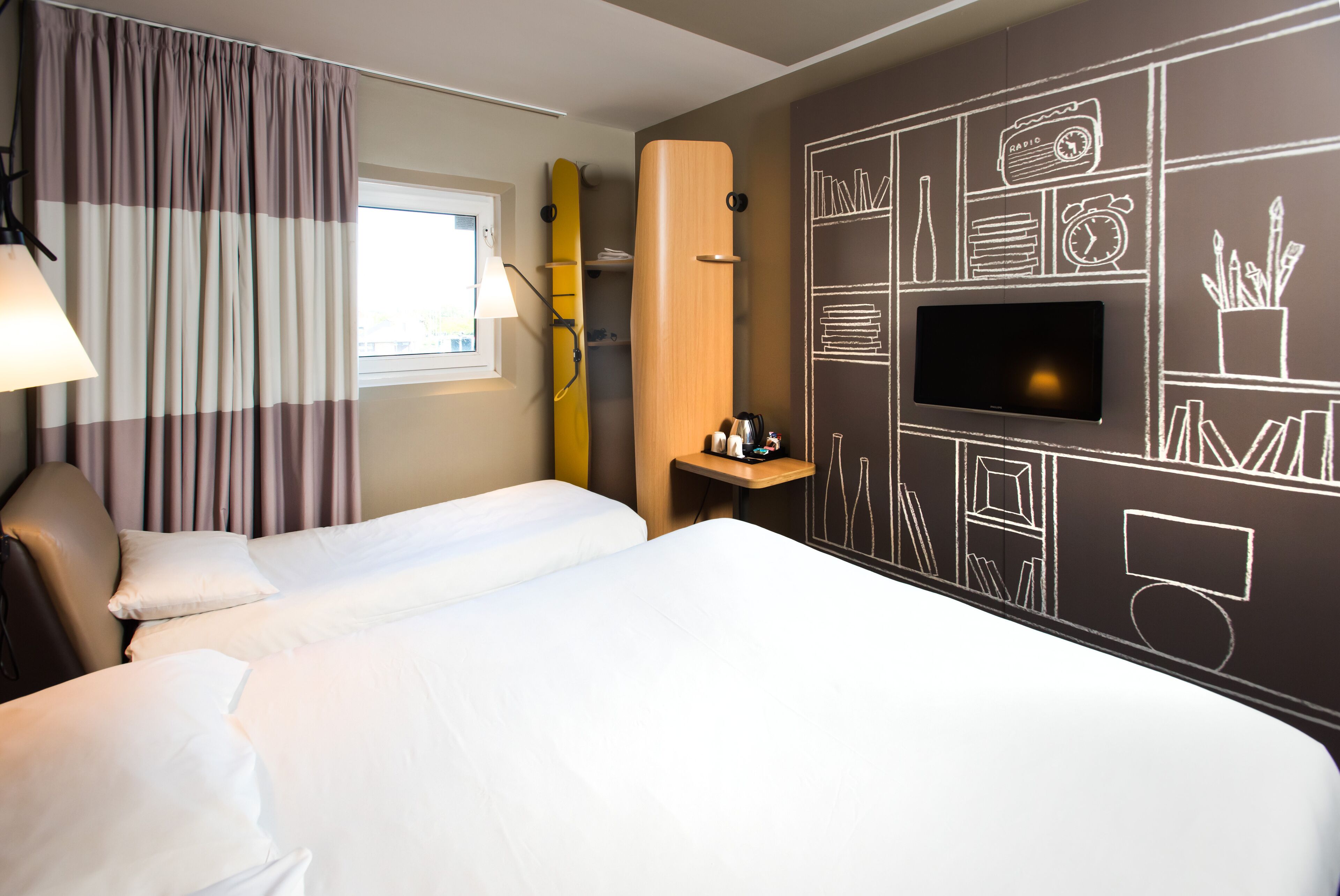 A hotel room with two beds, a TV, and a wall decorated with various icons.