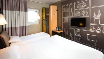A hotel room with two beds, a TV, and a wall decorated with various icons.